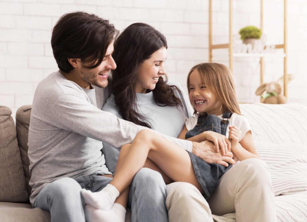 Loving parents tickling their little daughter, having fun together at home